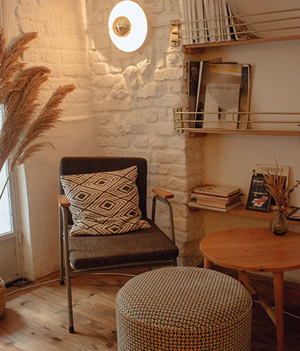 Een gezellige leeshoek met een zwart-witte fauteuil met geometrisch patroon, bijpassende ottomane en houten tafel. De achtergrond bestaat uit witte bakstenen muren, een lamp, planken met boeken, gedroogde planten in een vaas en pampasgras. Een gezellige leeshoek met een zwart-witte fauteuil met geometrisch patroon, bijpassende ottomane en houten tafel. De achtergrond bestaat uit witte bakstenen muren, een lamp, planken met boeken, gedroogde planten in een vaas en pampasgras.