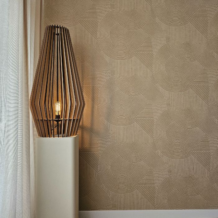 Een moderne lamp met een geometrisch houten kooiontwerp met een enkele gloeilamp is geplaatst op een strak wit voetstuk. De achtergrond, die doet denken aan het ingewikkelde penseelwerk van schilders, toont een beige muur met een gestructureerd patroon van overlappende bogen en lijnen, wat diepte en visuele interesse toevoegt.