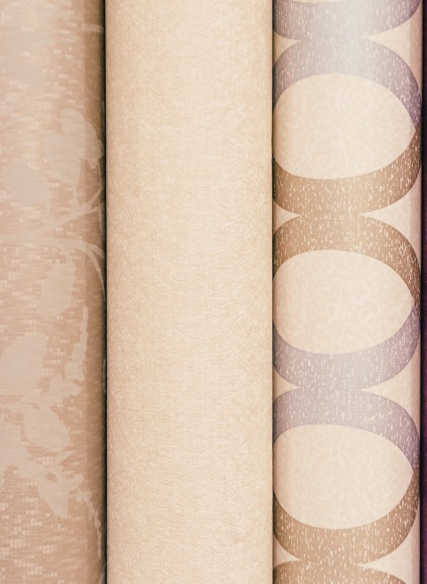 Vier rollen behang staan verticaal naast elkaar. Van links naar rechts: eerst een beige behang met een abstract bloemenpatroon; ten tweede een effen lichtbeige; ten derde een crèmekleur; en ten vierde een ontwerp met grote beige cirkels die met elkaar verbonden zijn door bruine ovalen en zilveren accenten die doen denken aan schildersdoeken.
